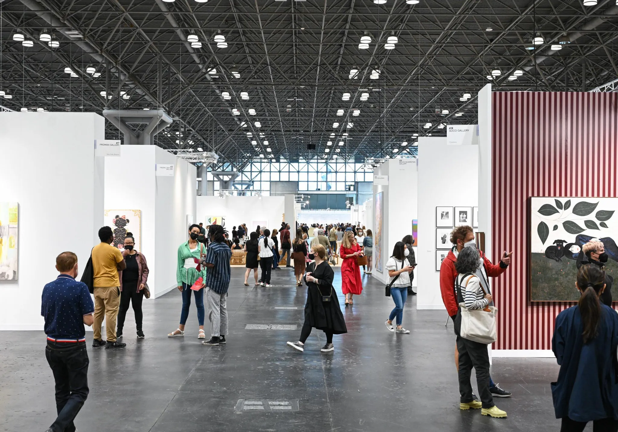 Visitors walking through a large exhibition hall with gallery booths inside the Javits Center in New York City.