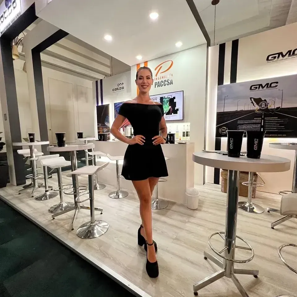 Attractive promotional model in a black dress standing inside a modern corporate trade show booth