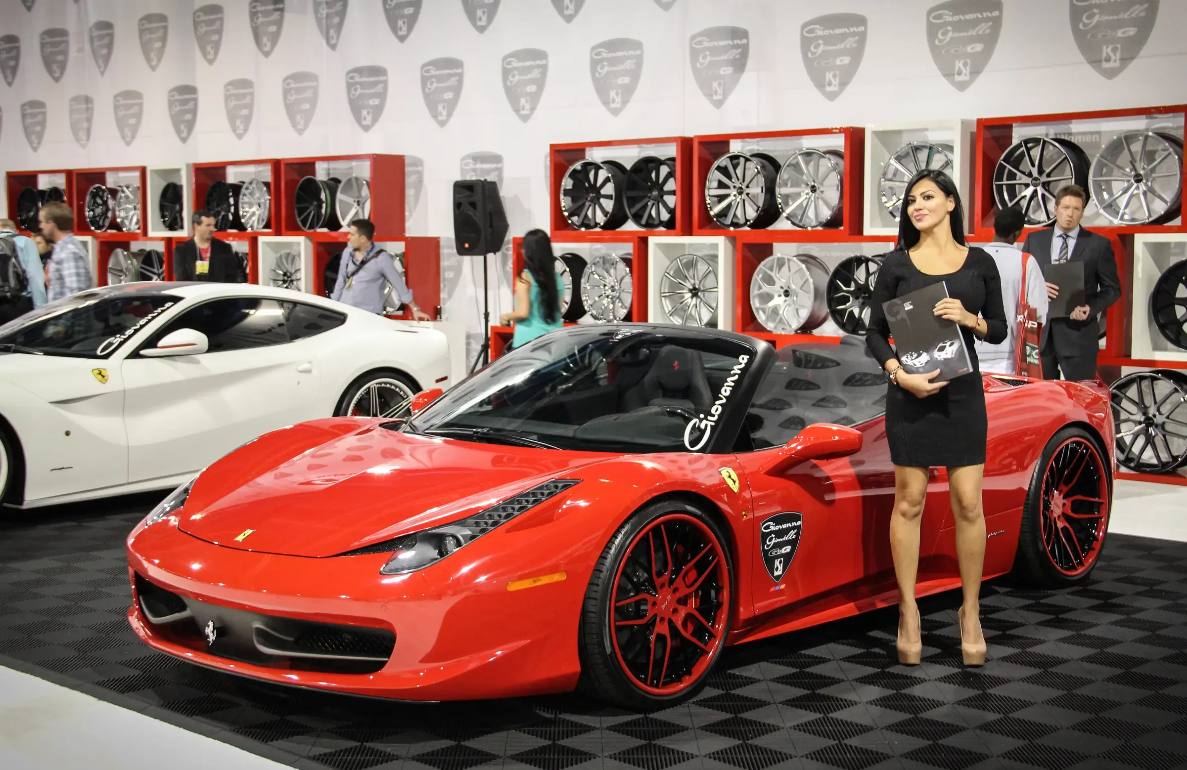 Promotional model beside a red Ferrari at the crowded SEMA Show exhibit floor in Las Vegas