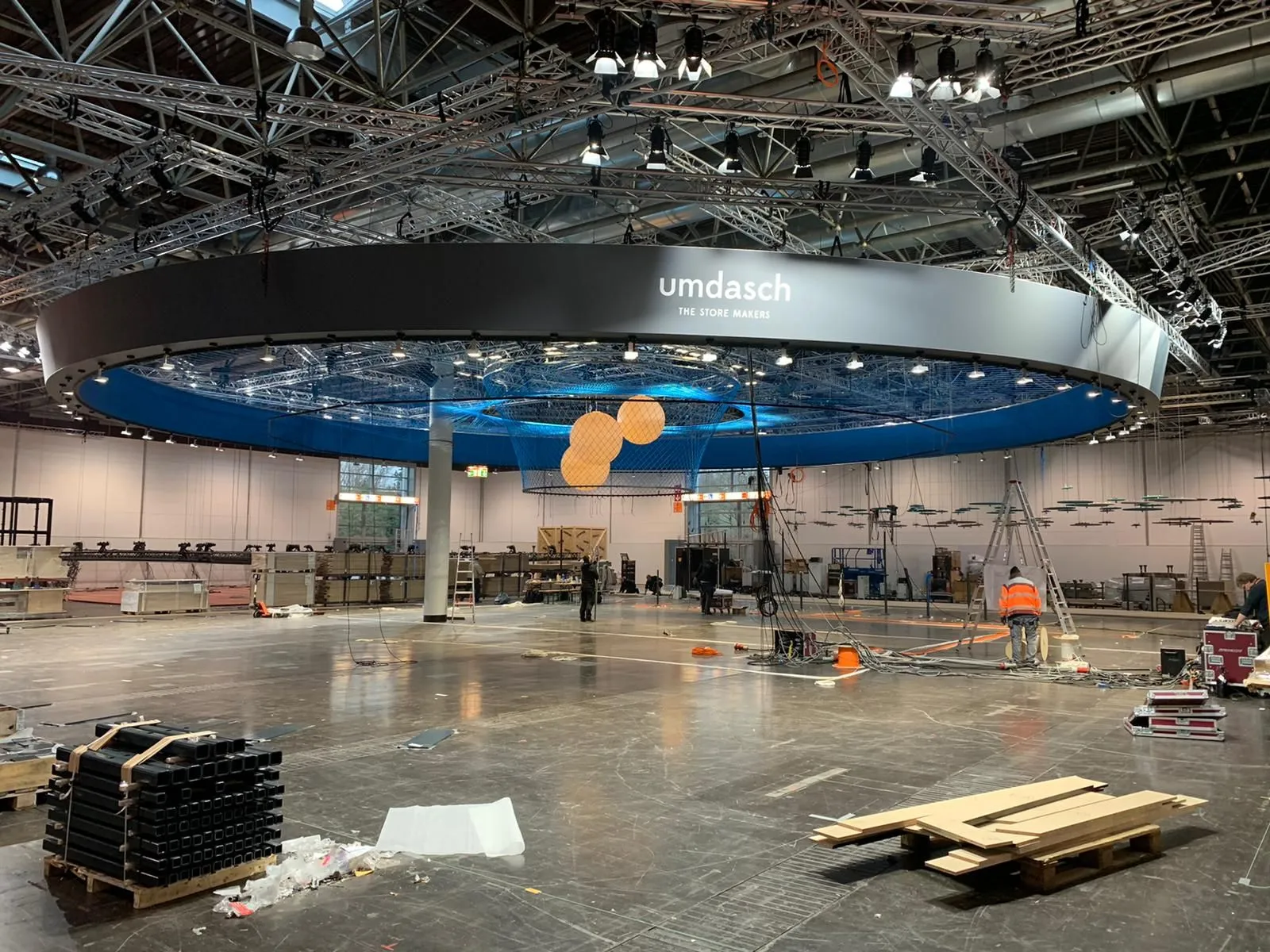 Installation crew assembling a massive illuminated overhead booth structure on the trade show floor | Purple Exhibits