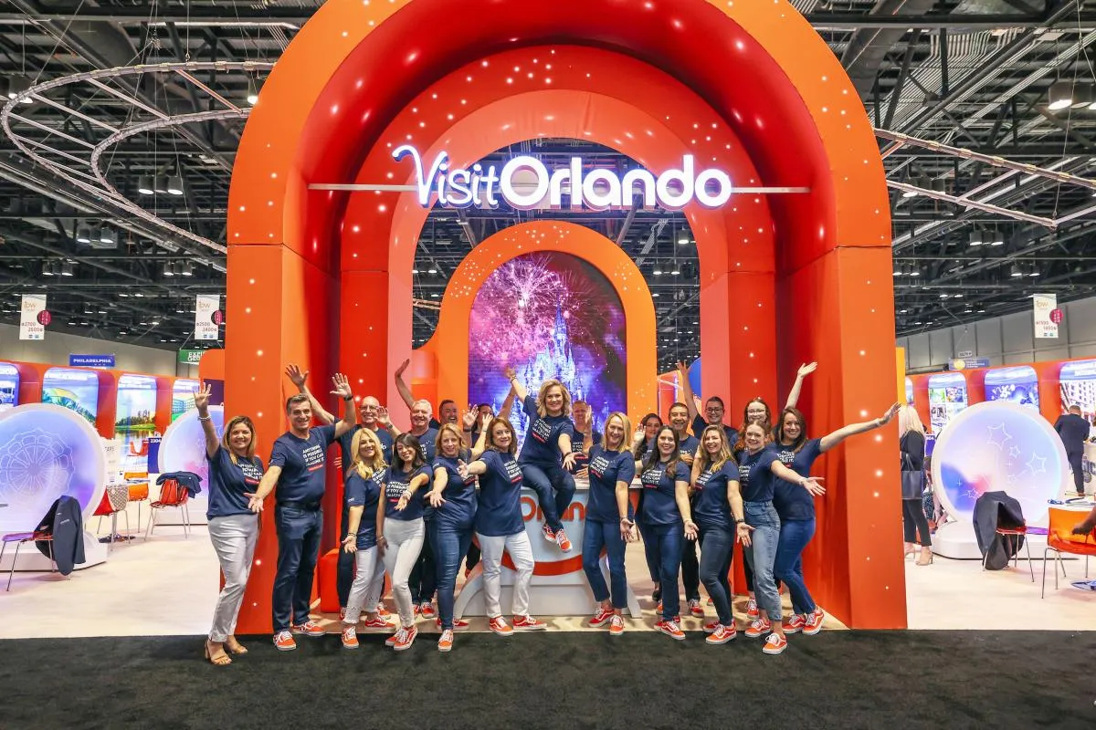 Large illuminated Visit Orlando exhibit with colorful destination graphics and a professional female brand team
