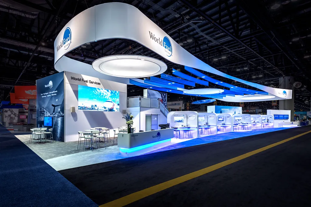 Large custom trade show exhibit booth with illuminated displays, meeting spaces, and an open layout.