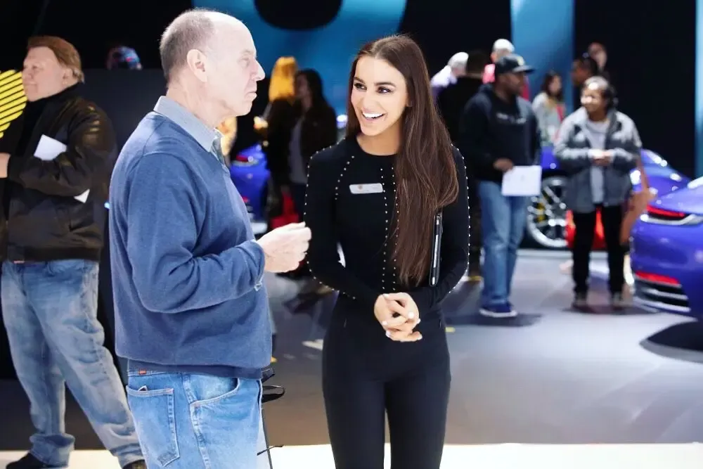 Attractive trade show model speaking with an attendee at a busy automotive business exhibition
