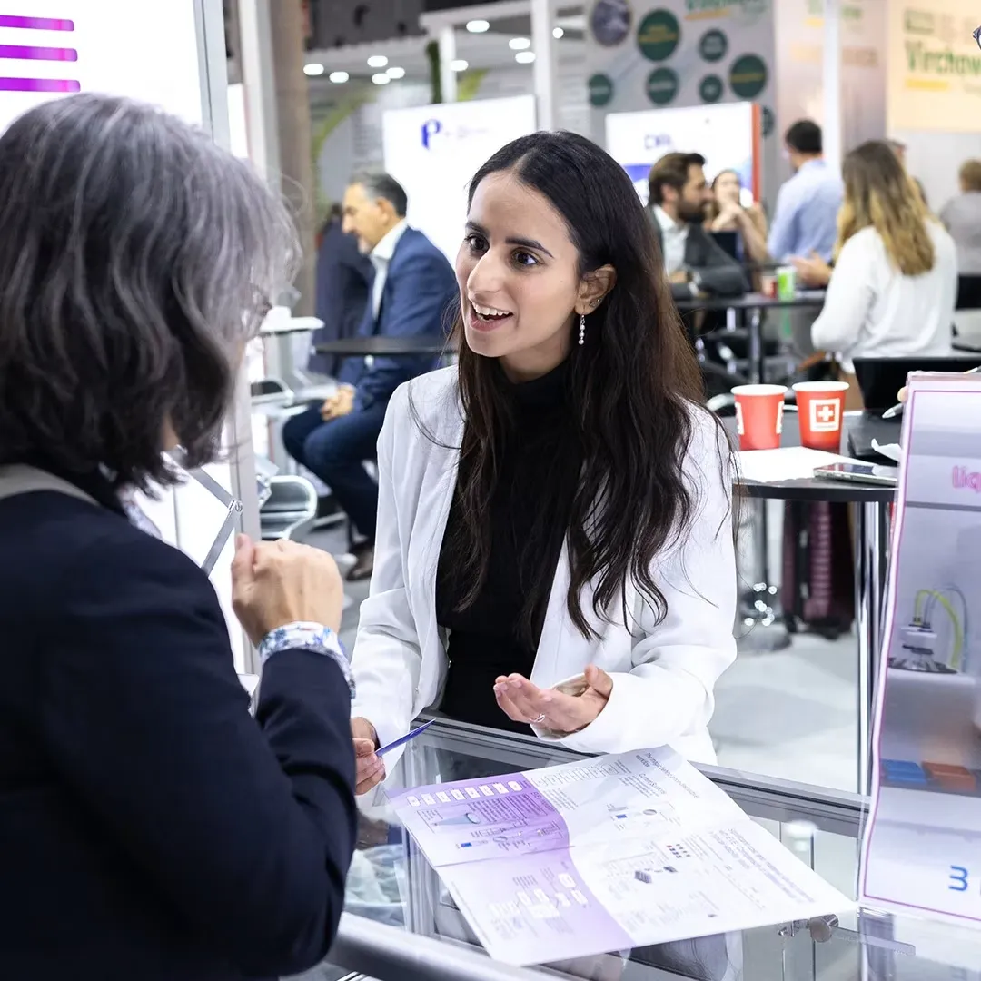 Attractive professional female trade show representative confidently engaging an attendee inside an exhibit booth