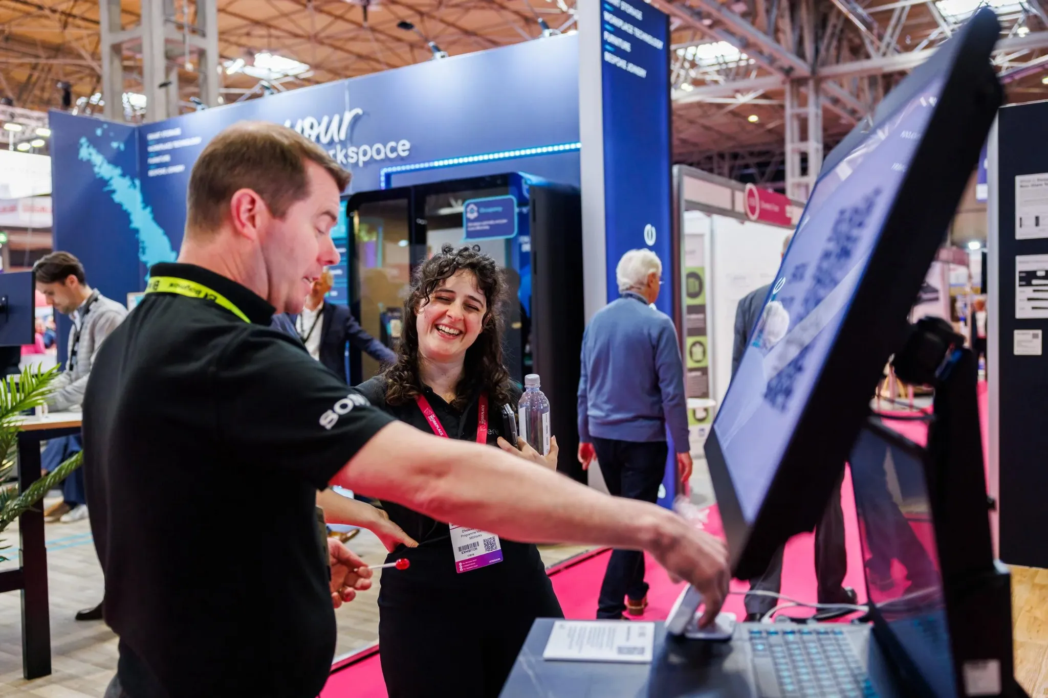 Exhibitor presenting an interactive product demonstration to an attendee at a technology trade show booth.