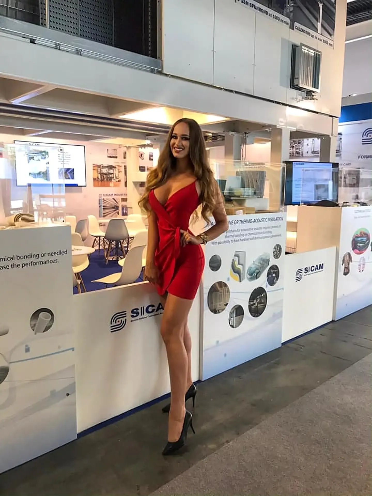 Promotional model in a red dress standing inside a modern trade show exhibit booth