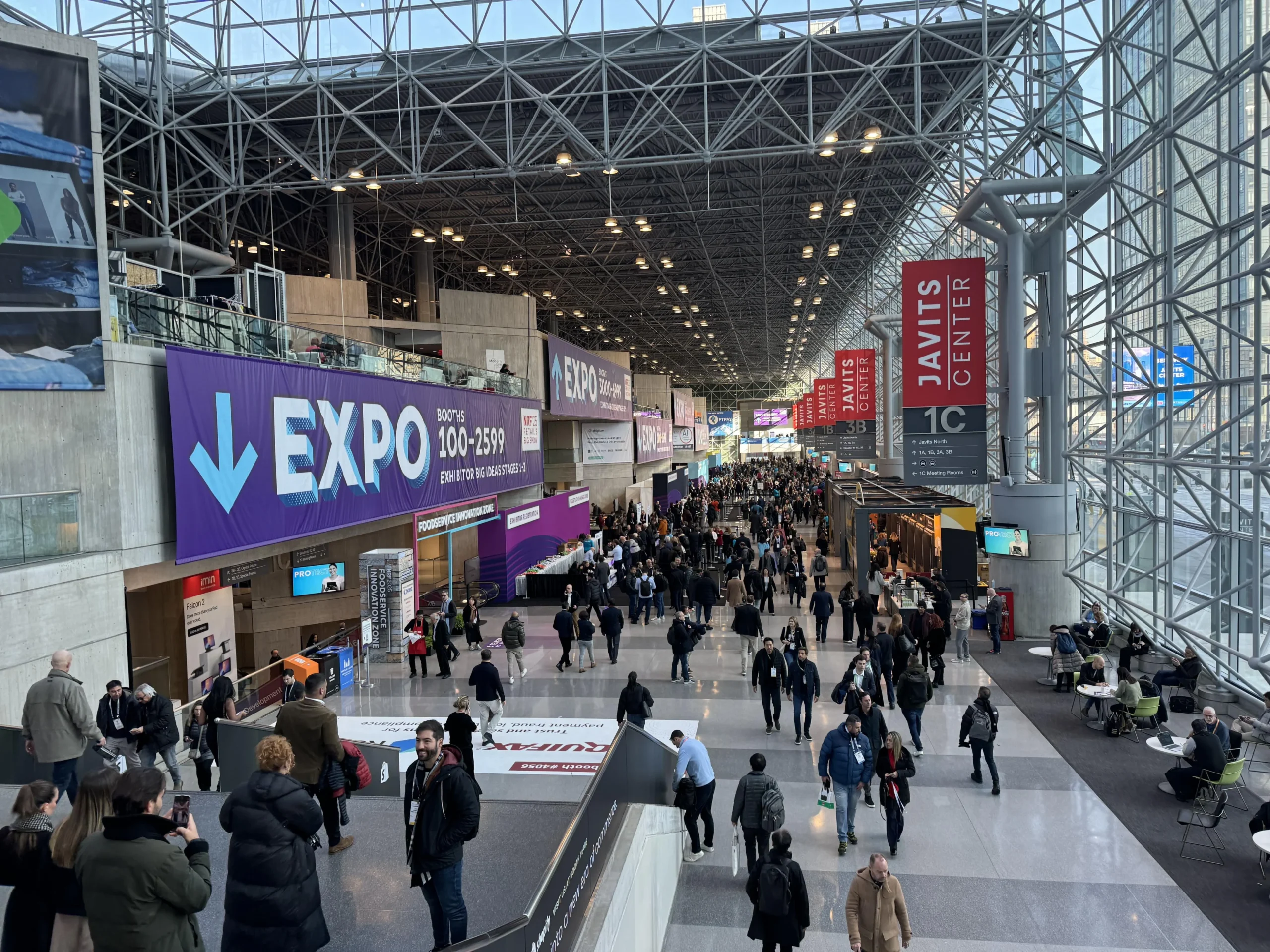 Busy trade show floor with modern exhibit booths and attendees inside the Javits Center in New York City.