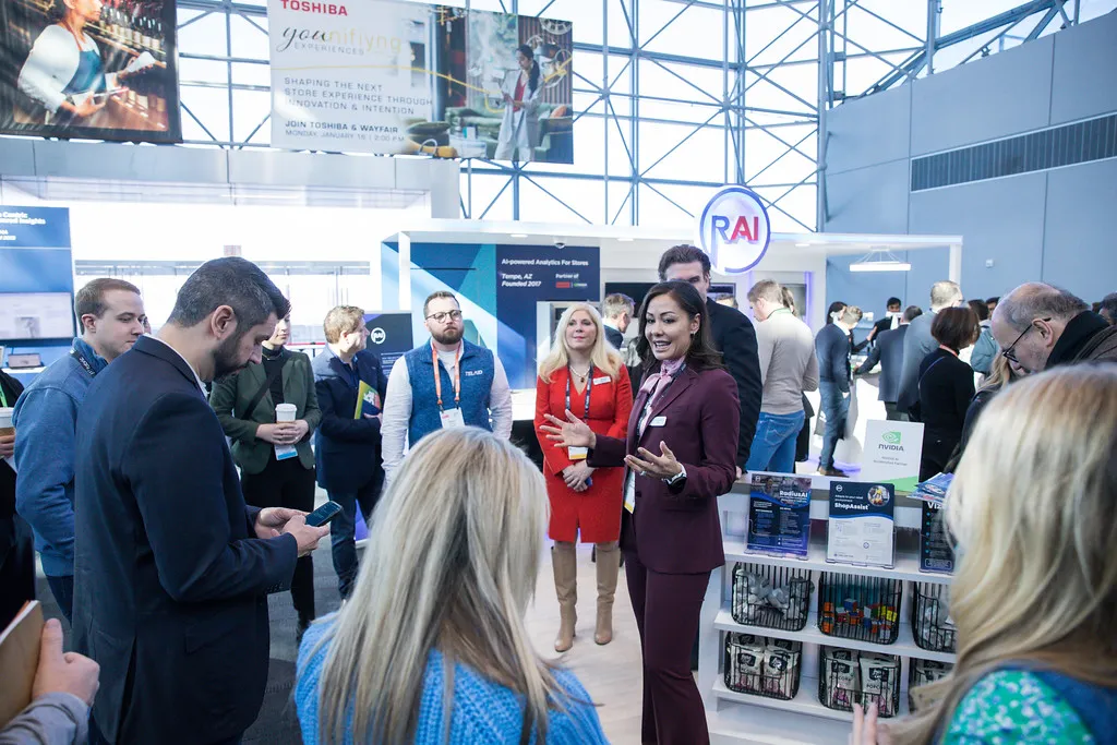Female presenter engaging attendees inside a large technology exhibit booth at NRF Retail’s Big Show.