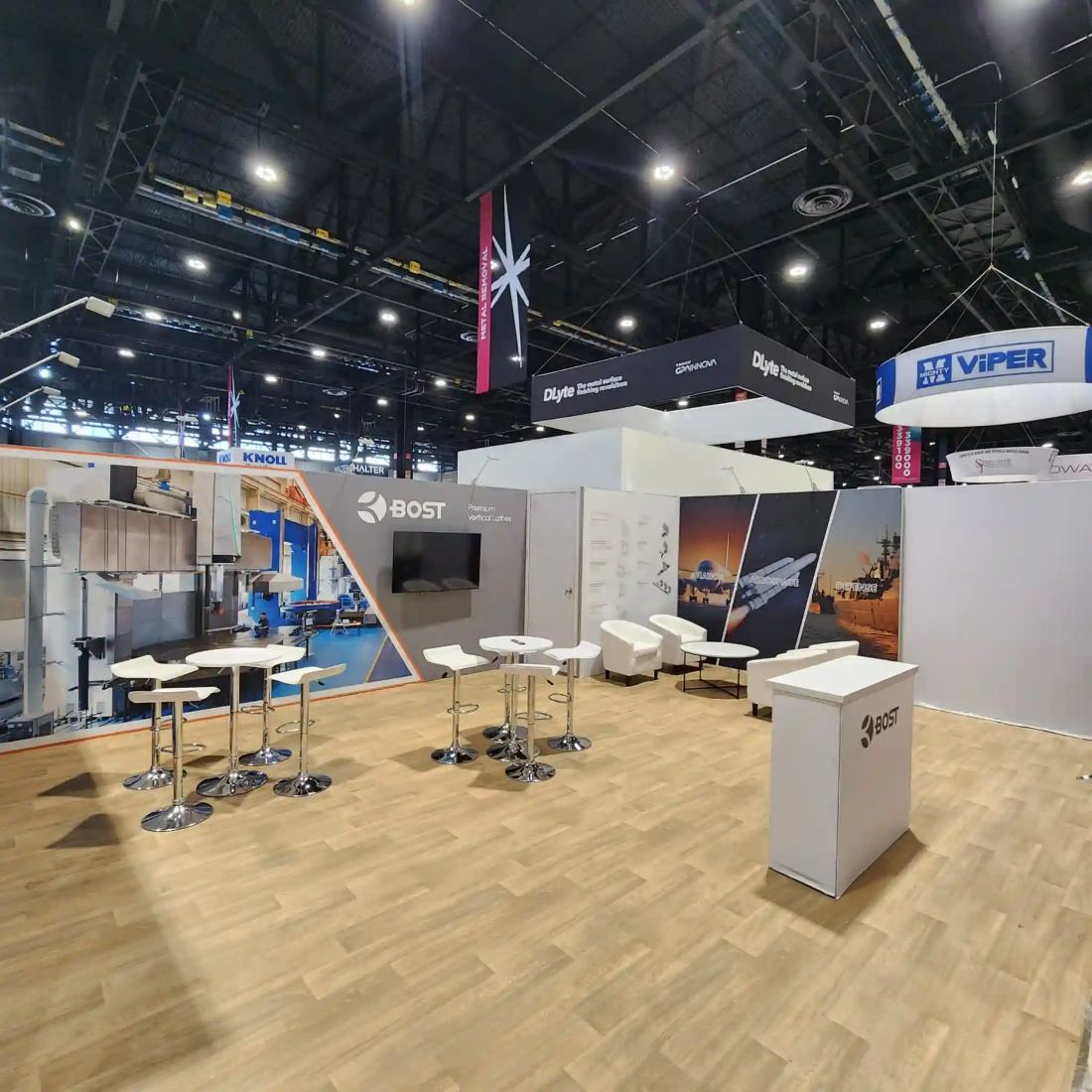 BOST 20x30 island trade show exhibit with hanging signs, large-format machinery graphics and lounge seating