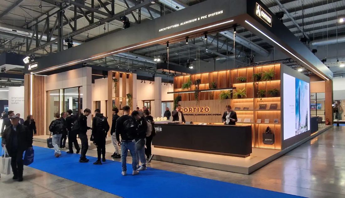 Cortizo 40x40 island exhibit with a black overhead canopy, full-scale window and door displays, reception counter and LED wall