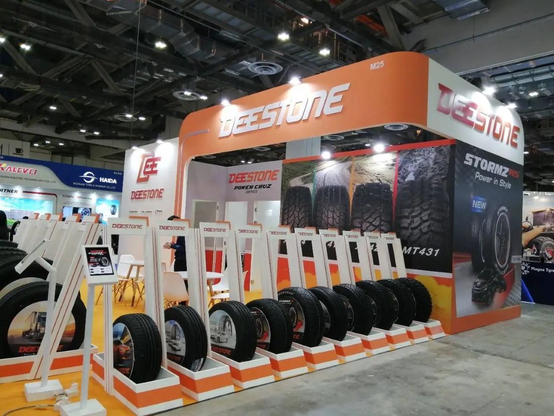 Deestone 30x40 island trade show exhibit with an orange curved header, large-format tire graphics and a row of product stands