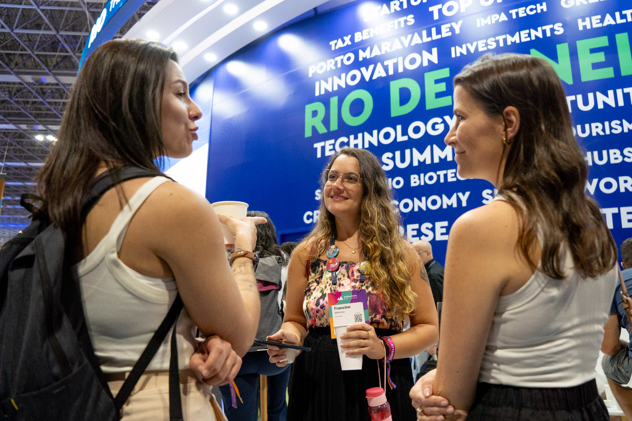 Three women making connections beside the Invest.Rio exhibition booth