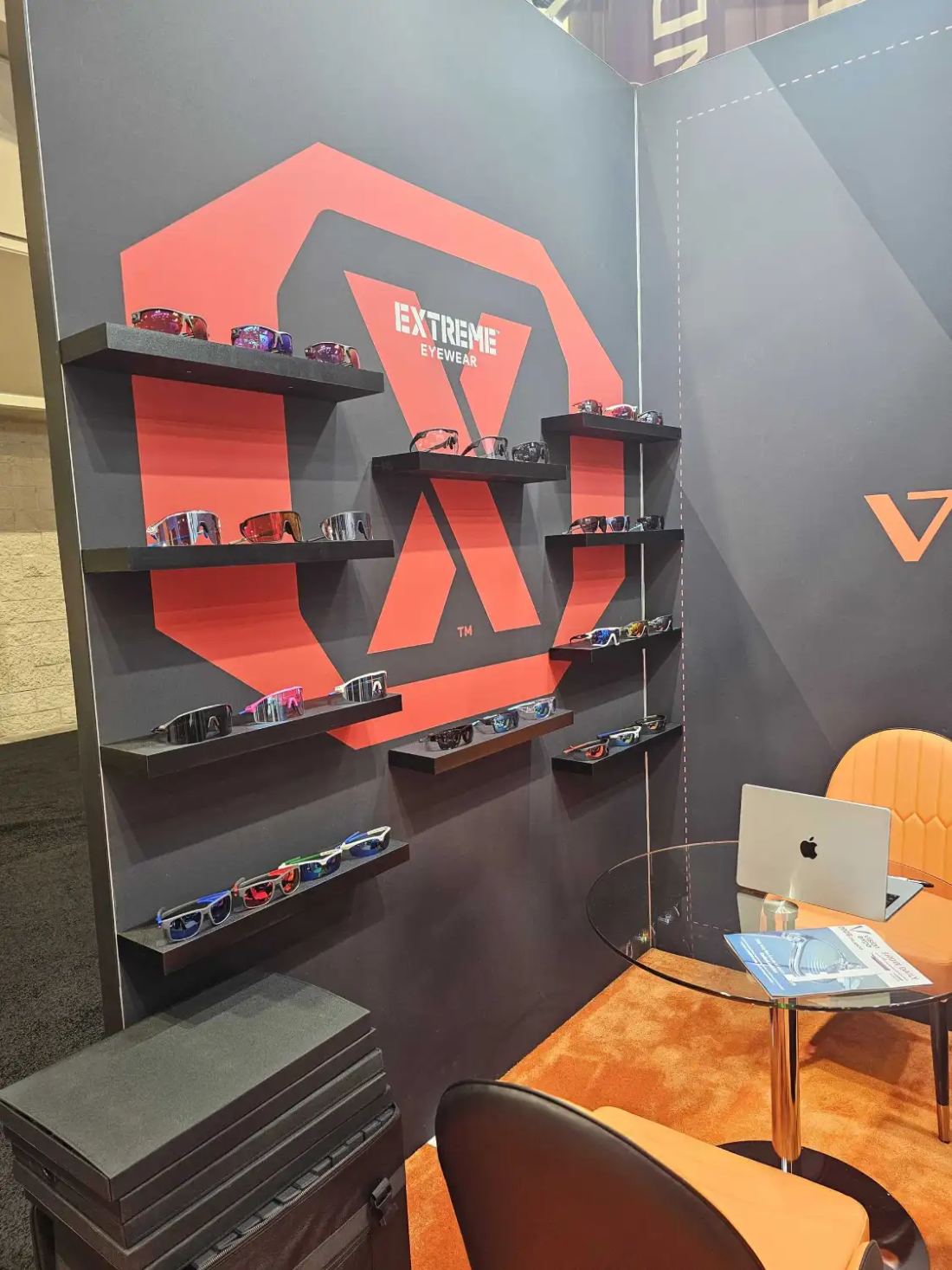 Extreme Eyewear 10x10 inline trade show booth with a red and charcoal graphic wall, floating product shelves and a meeting table