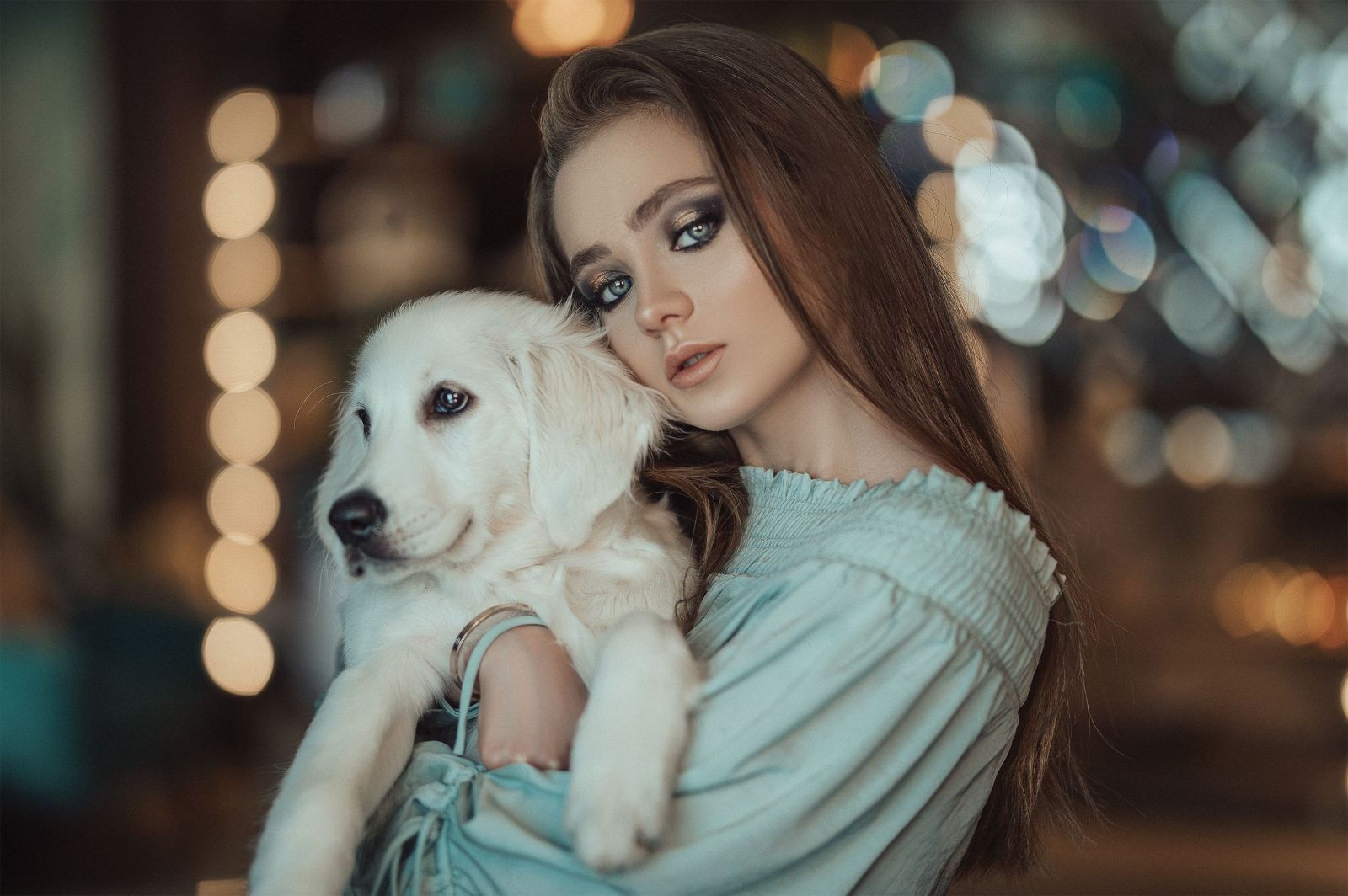 Fashionable woman embracing a golden retriever puppy against soft bokeh lights