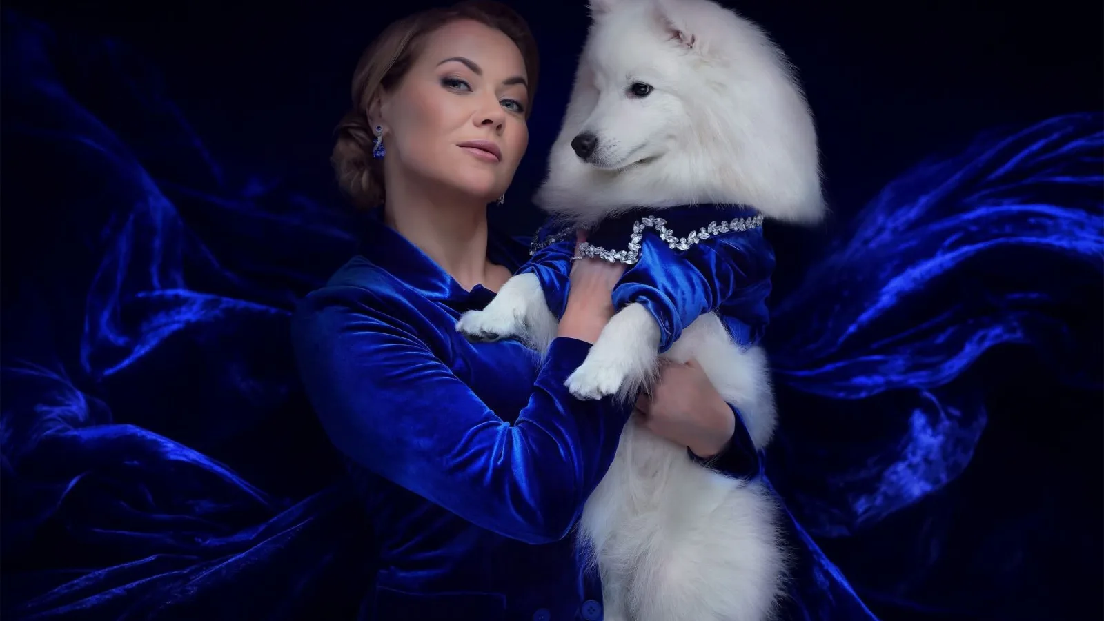 Elegant woman in blue velvet holding a white Samoyed dog