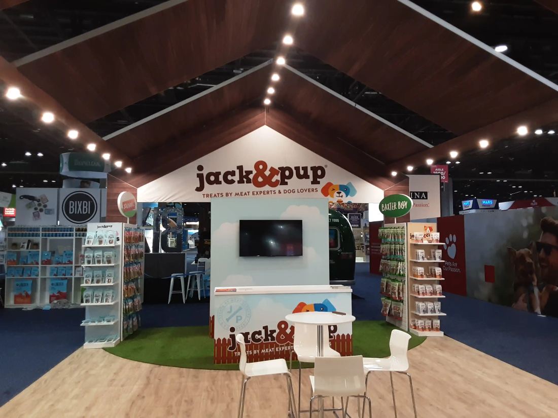 Jack and Pup 20x30 island trade show booth with a gabled wood roof, retail product shelving and turf flooring