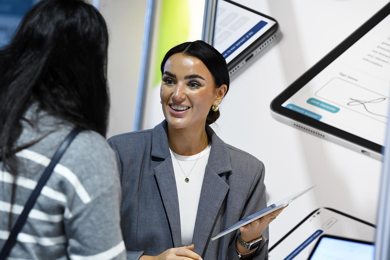 Booth team member holding a tablet while talking a visitor through digital planning screens