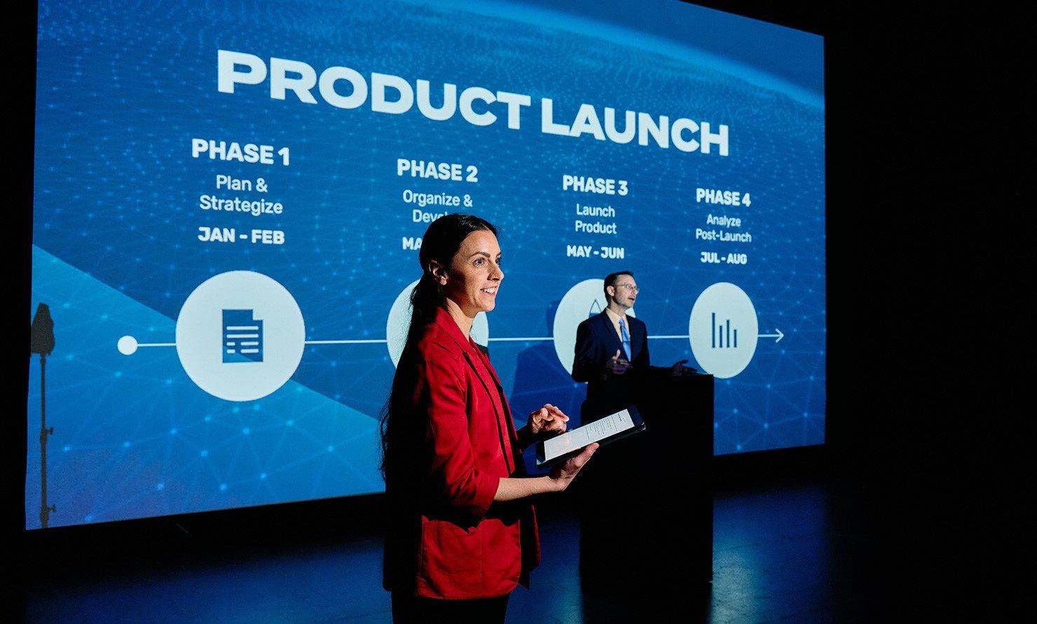 Product launch phase timeline projected on a large screen behind two presenters on stage