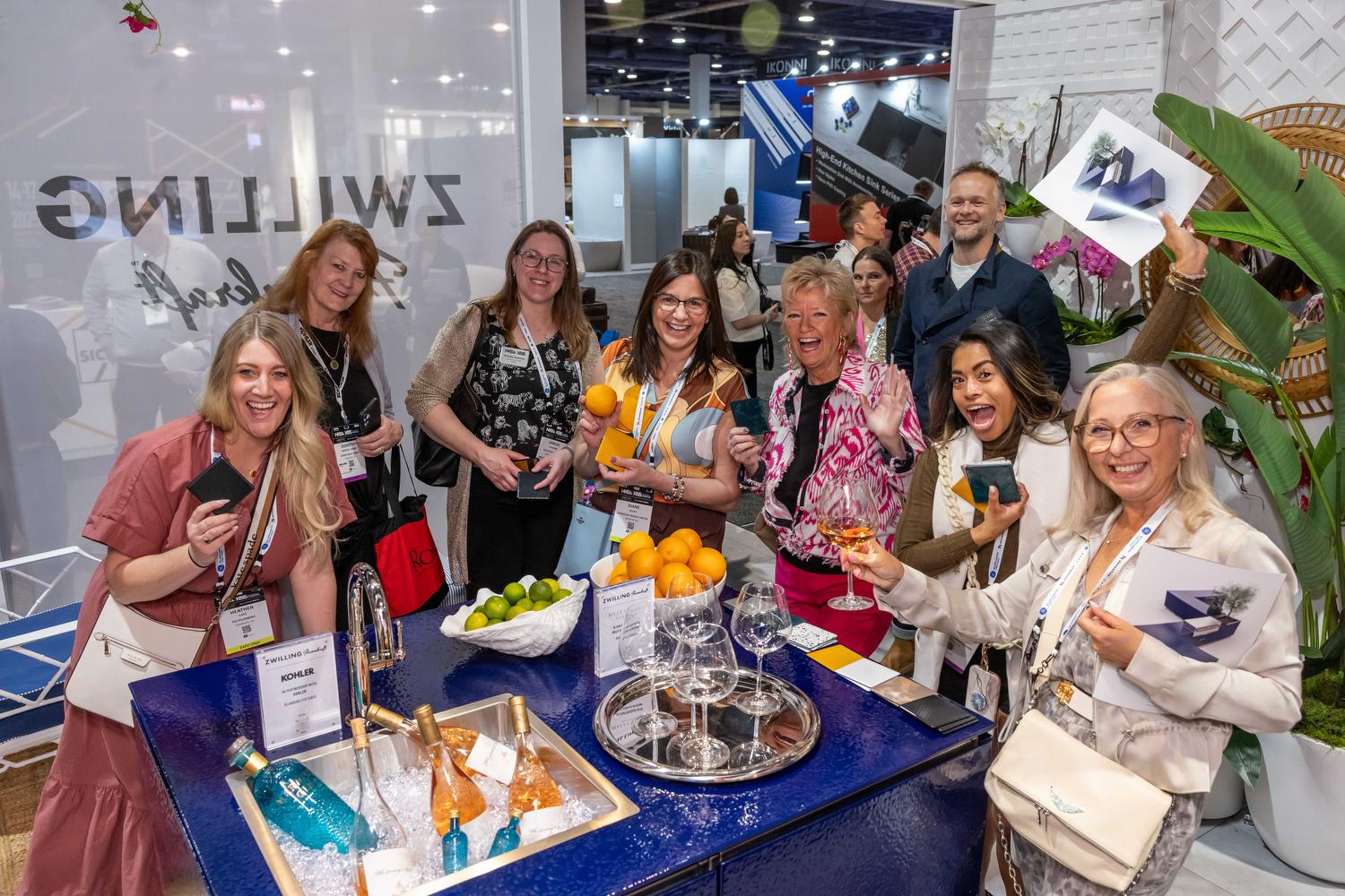 Booth staff welcoming a group of engaged visitors at a hospitality bar inside a KBIS exhibit