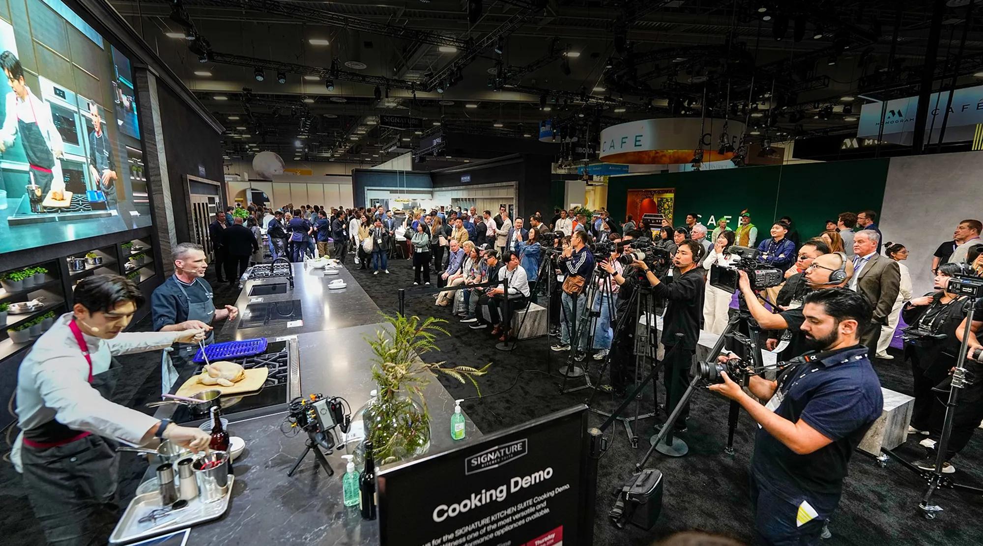 Live cooking demonstration at a KBIS appliance booth drawing a seated audience and press cameras