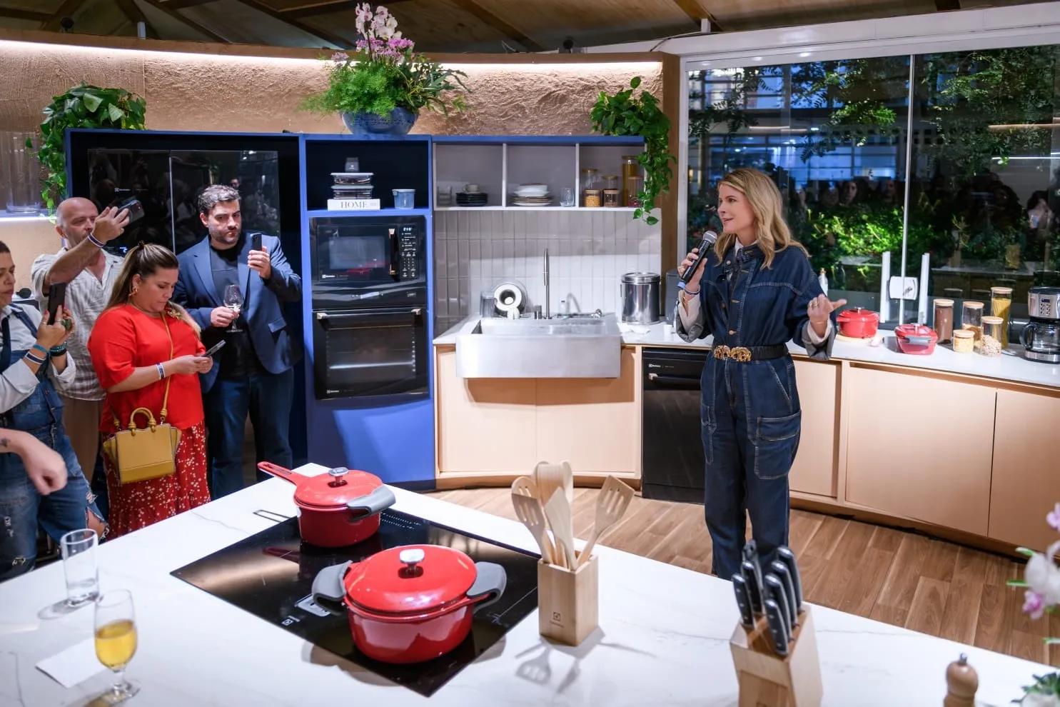 Presenter speaking to an invited audience inside a working kitchen display at a trade show launch event