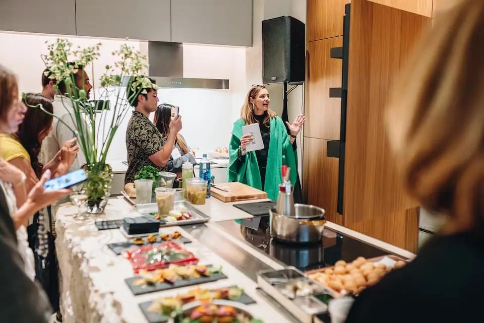 Presenter running a live kitchen demonstration while attendees film and photograph the result