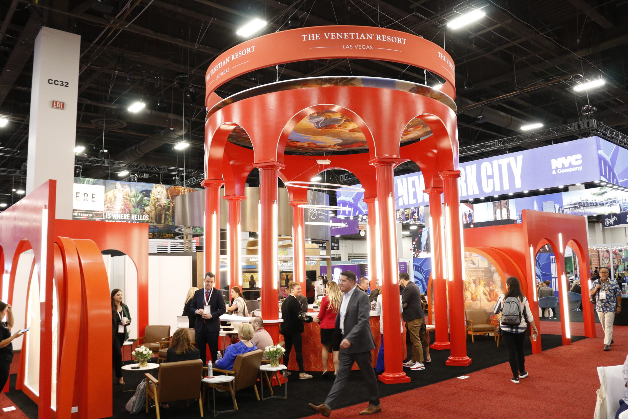 Exhibitors and show staff meeting inside a large red columned exhibit on a Las Vegas show floor, with neighbouring destination booths behind