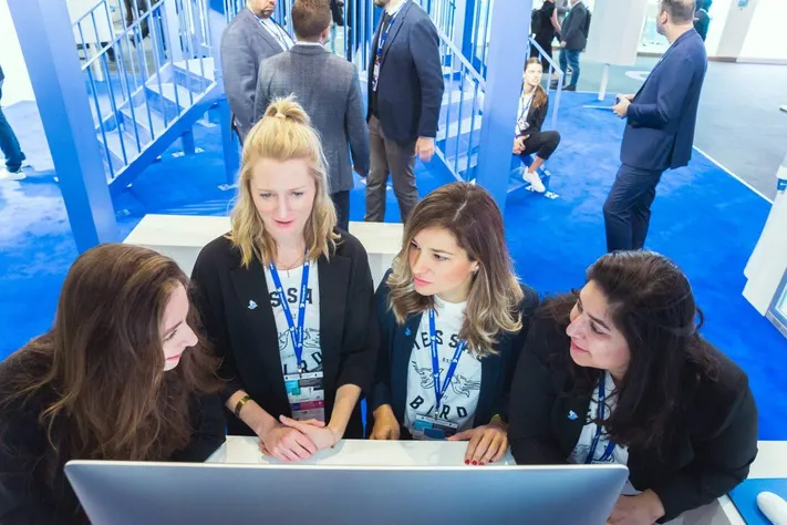Four exhibit team members reviewing a shared screen together on a show floor stand
