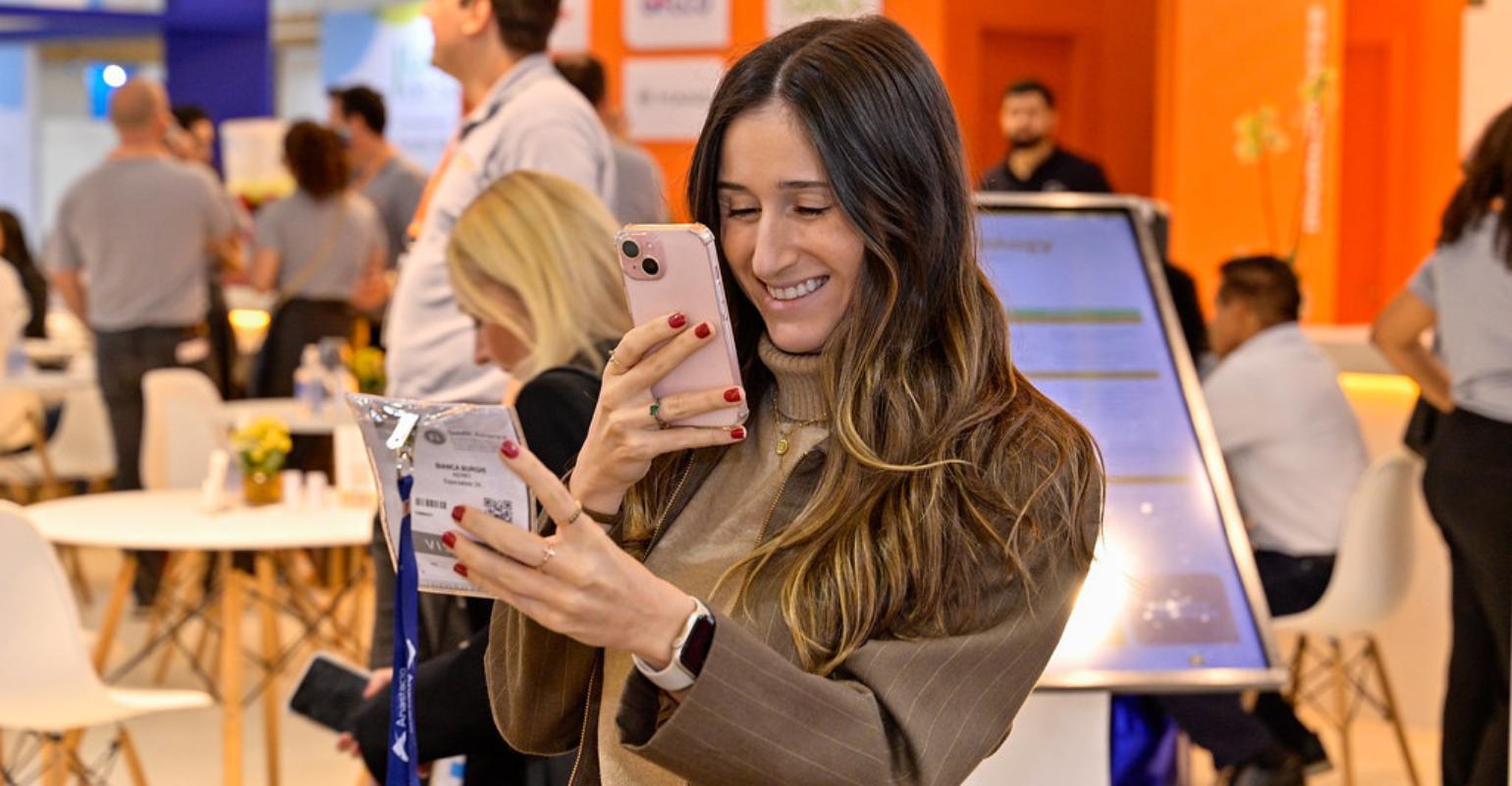 An event attendee holds her badge and checks her phone in an exhibition networking area.