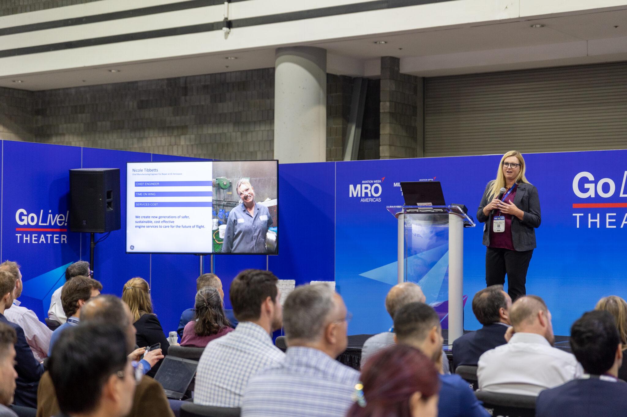 A presenter speaks to a seated audience at the Go Live! Theater at MRO Americas, with a slide about engine services on screen.