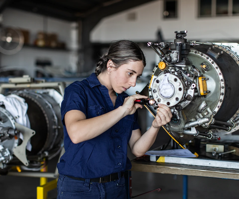 An aviation technician inspects an aircraft engine module with a flashlight in a maintenance workshop.