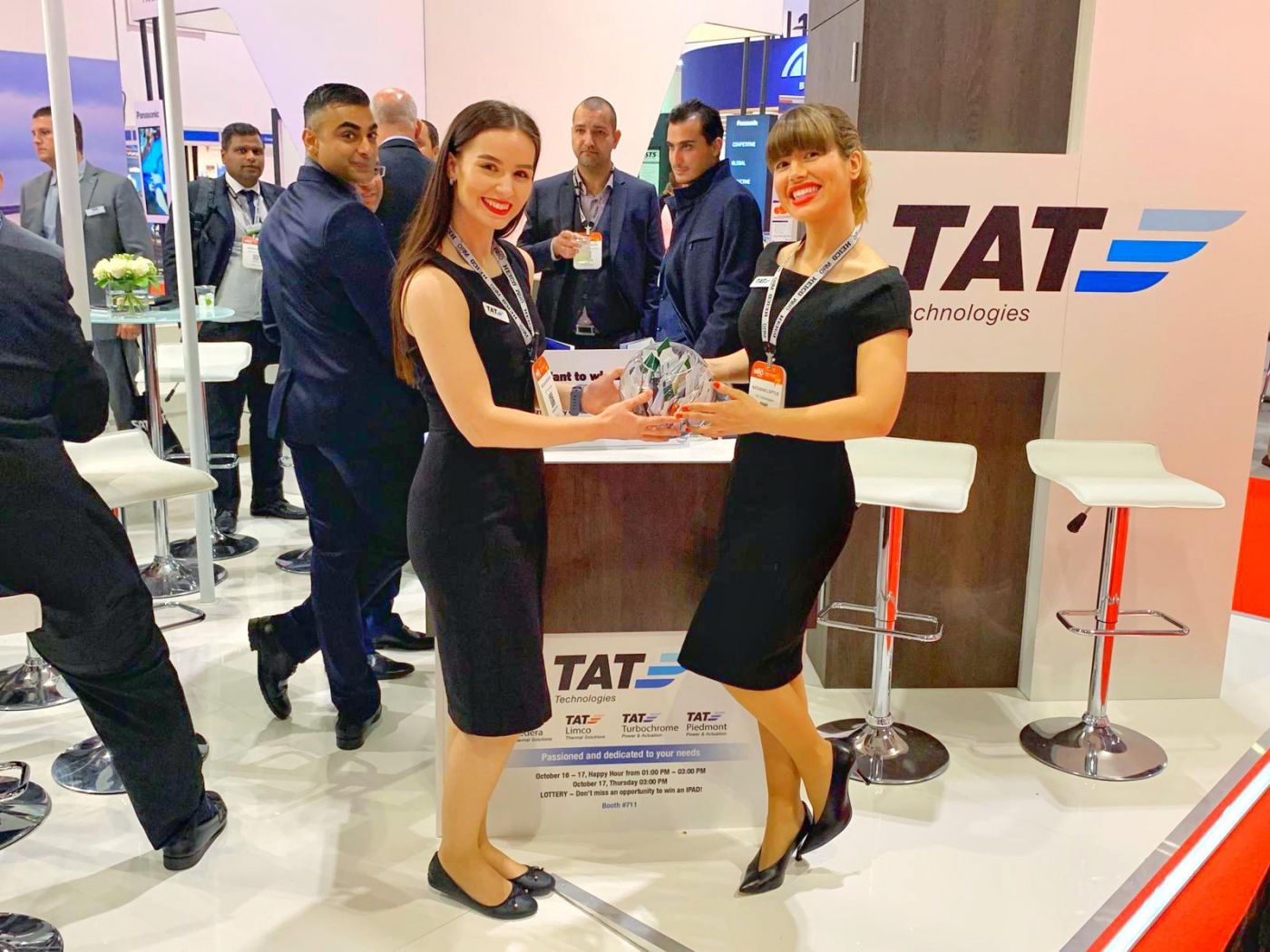 Exhibit staff greet arriving visitors beside a reception counter at an aviation trade show stand.