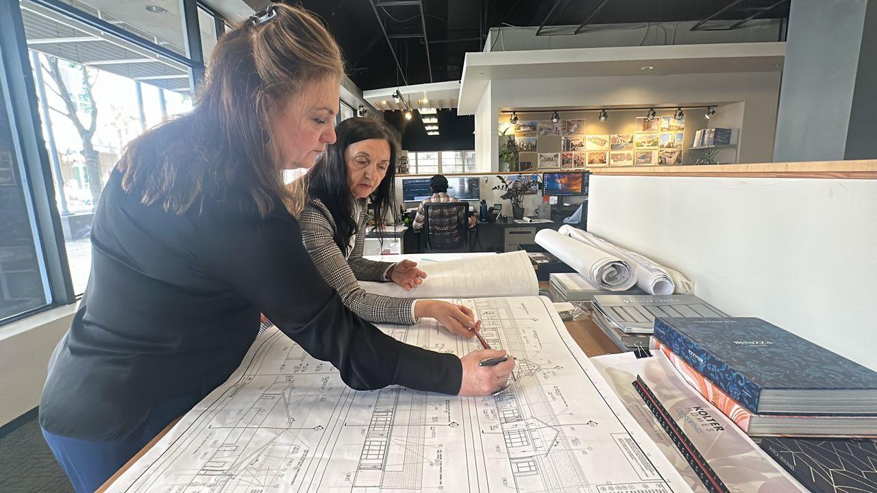 Two exhibit project team members reviewing a large scaled drawing set spread across a work table in a design studio.