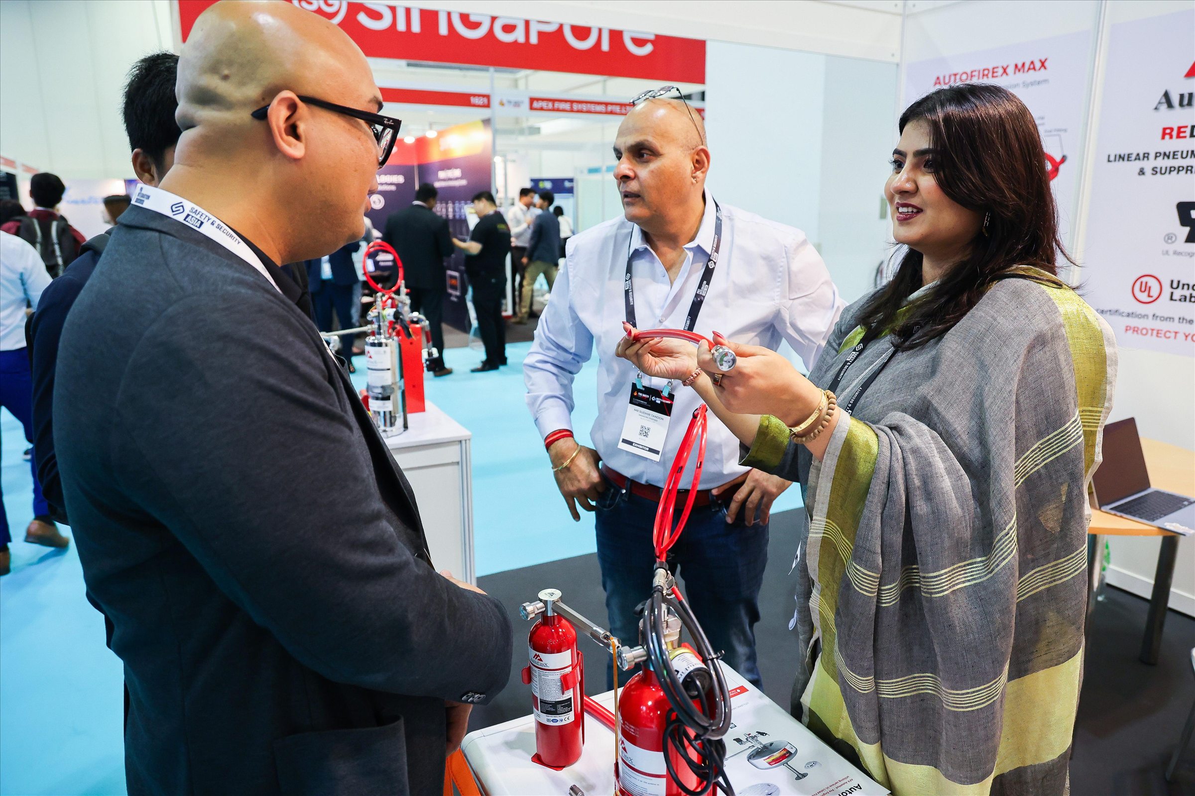 Exhibitors discussing fire-suppression cylinders and hose assemblies displayed on a trade show stand.