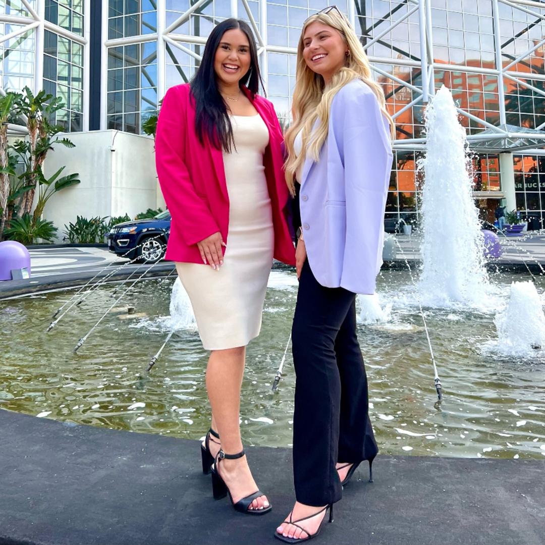 Two event professionals in blazers standing beside the fountain outside a glass-fronted convention center entrance.