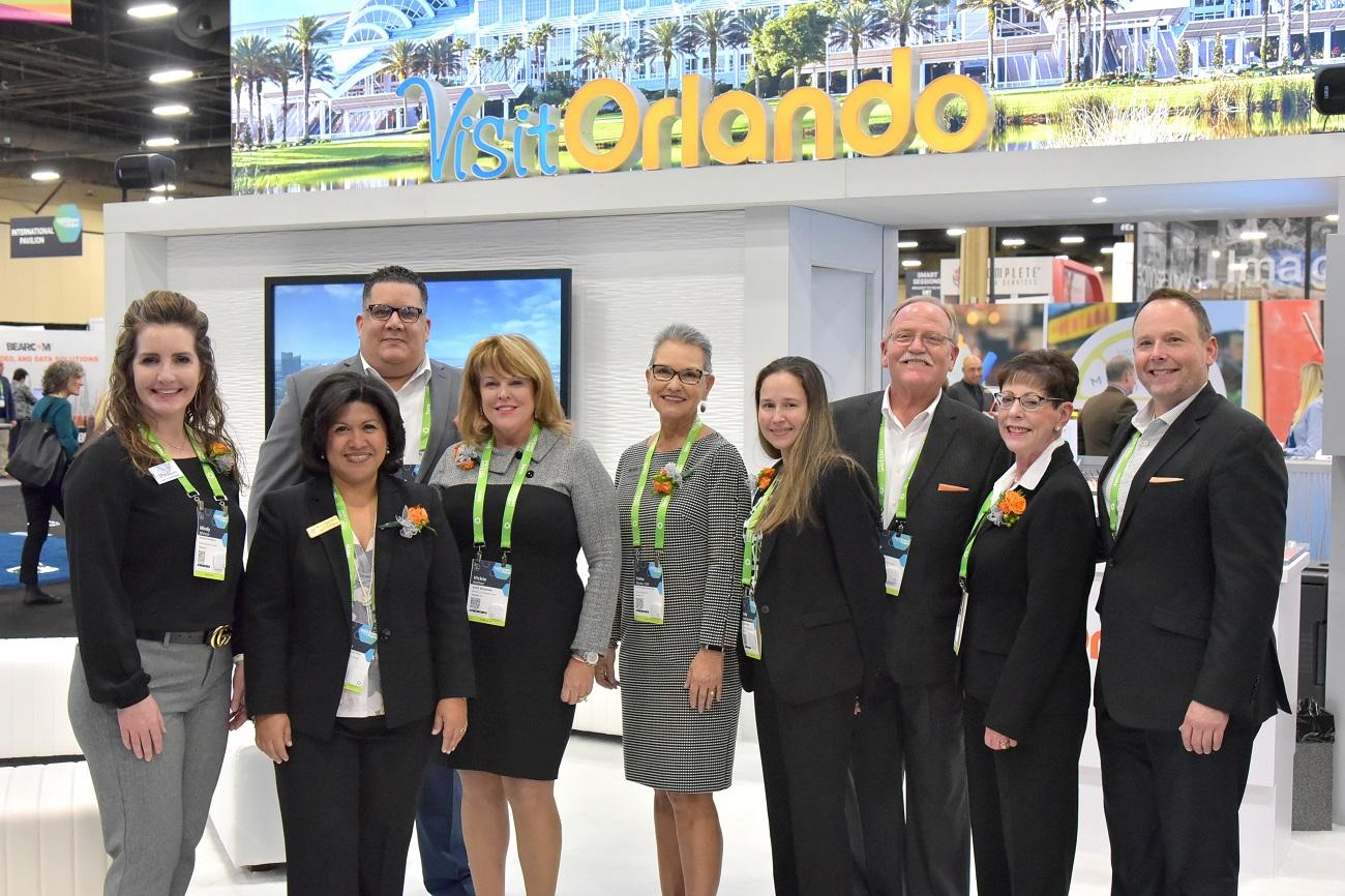 A destination and venue services team photographed together in front of their exhibit on a trade show floor.