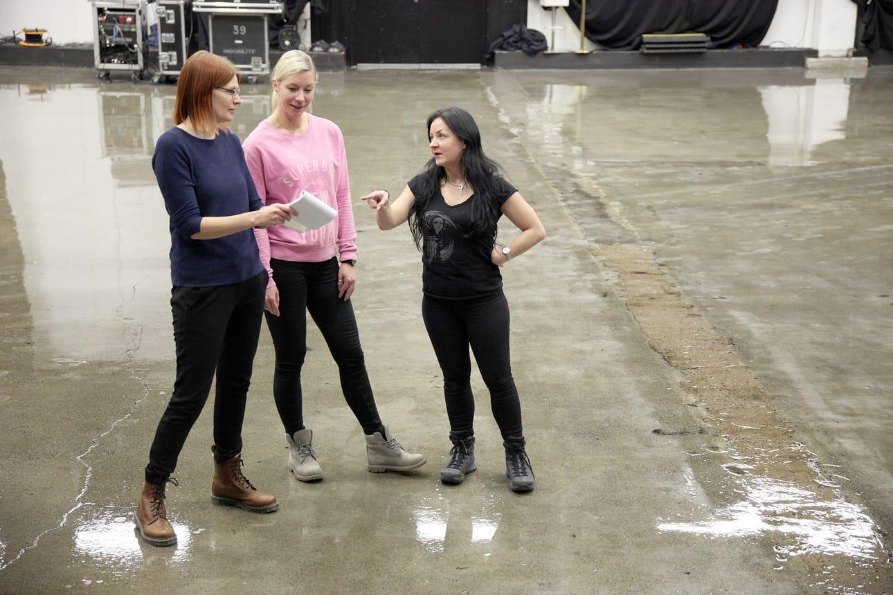 Three exhibit team members standing on an empty exhibit hall floor reviewing notes before installation begins.