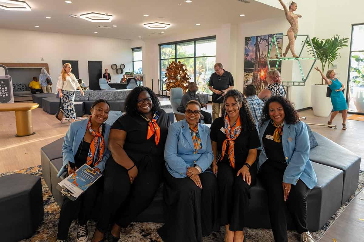 A group of convention center staff in matching blazers and scarves seated together in a venue lobby.