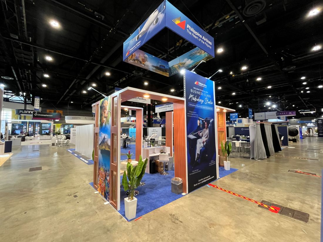 Philippine Airlines 20x20 island trade show exhibit with a hanging square sign, wood portals and lounge seating