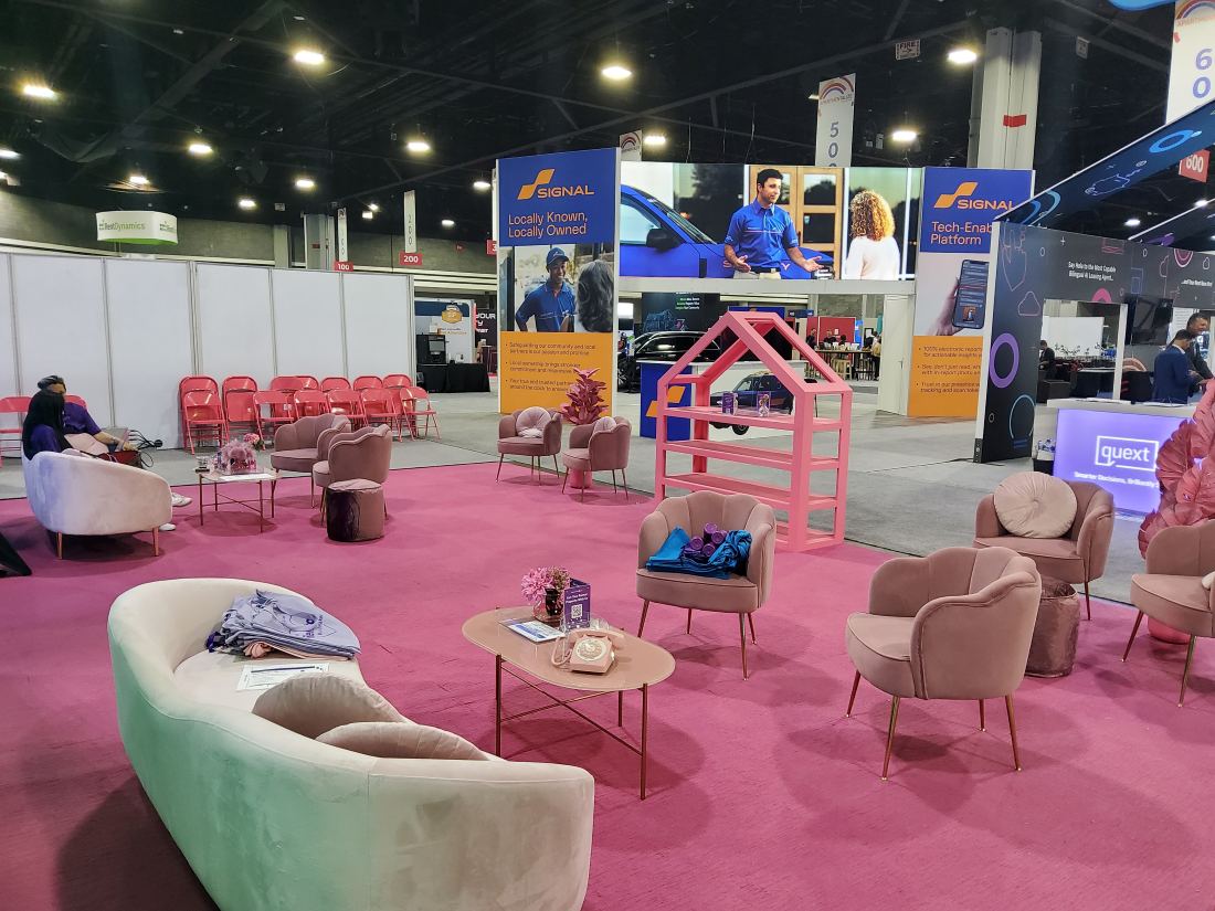 Signal 20x20 island trade show booth with pink lounge seating, planters and hanging sign