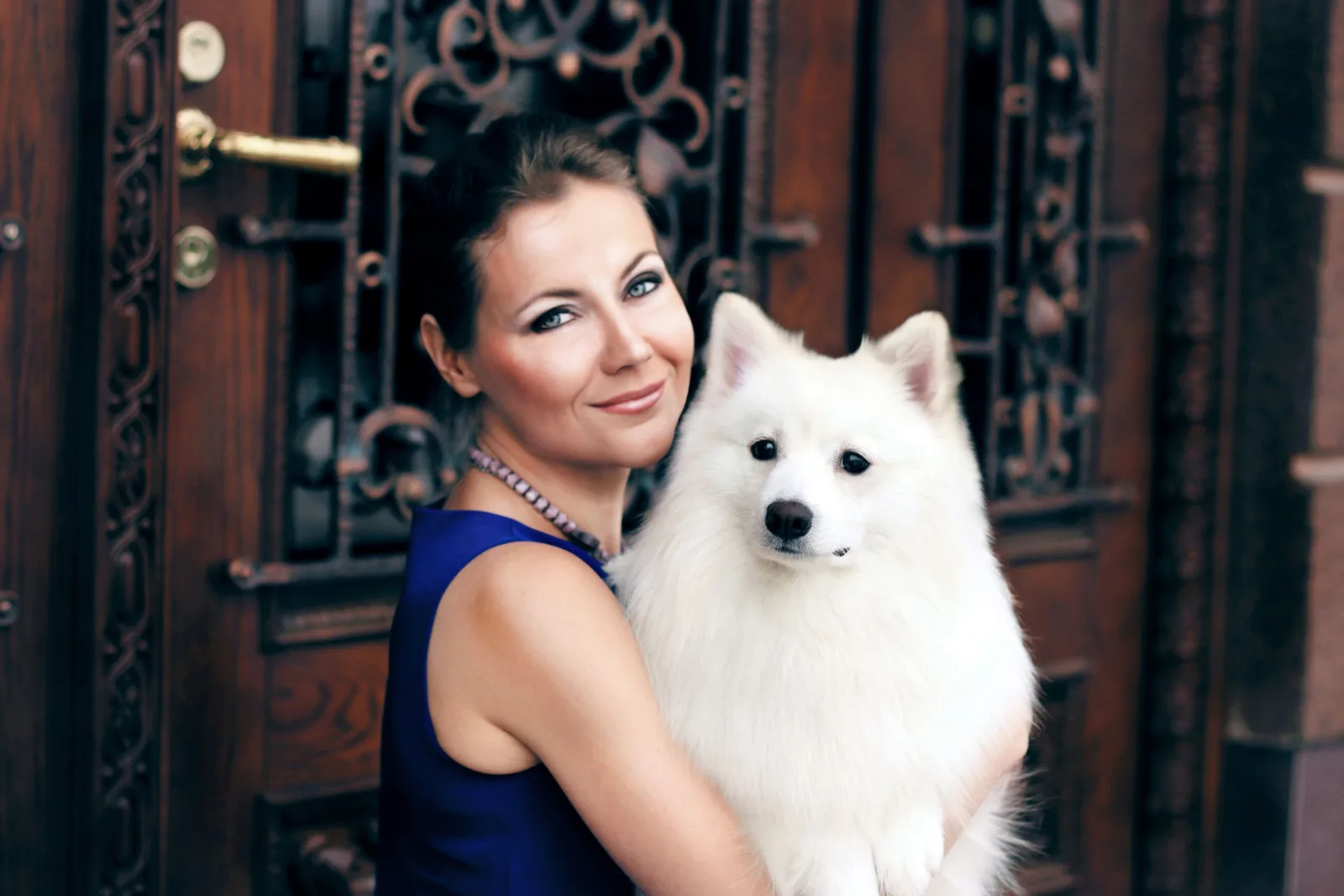 Smiling woman in a blue dress hugging a white Samoyed dog