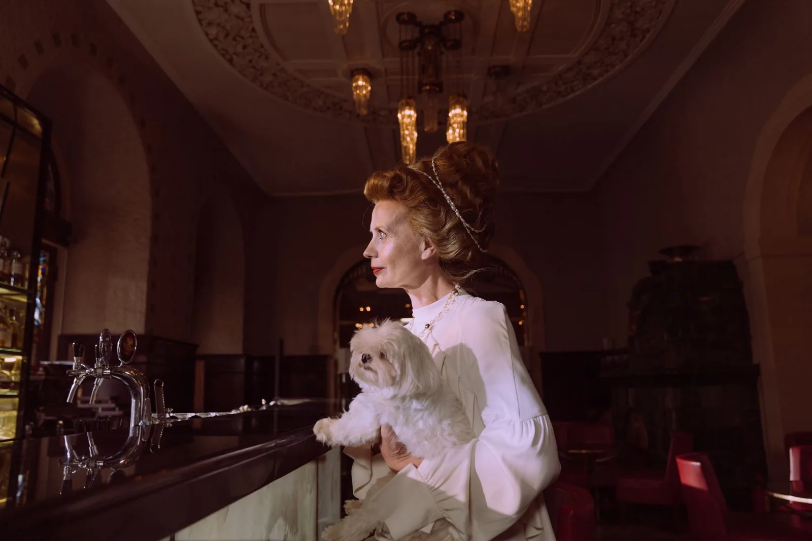 Sophisticated woman holding a Maltese dog in an ornate bar