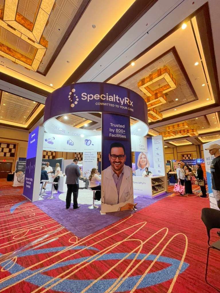 SpecialtyRx 10x10 inline trade show booth with curved header, purple carpet and tower graphic