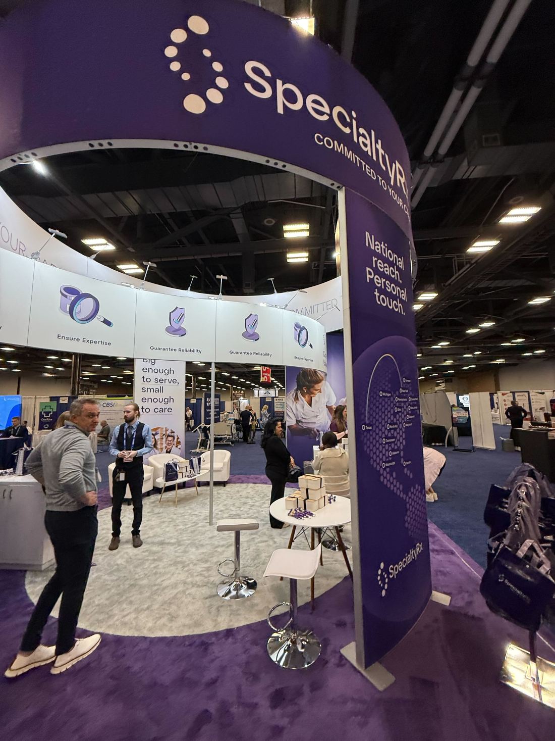 SpecialtyRx 10x20 inline trade show exhibit with a round purple LED tower and curved header