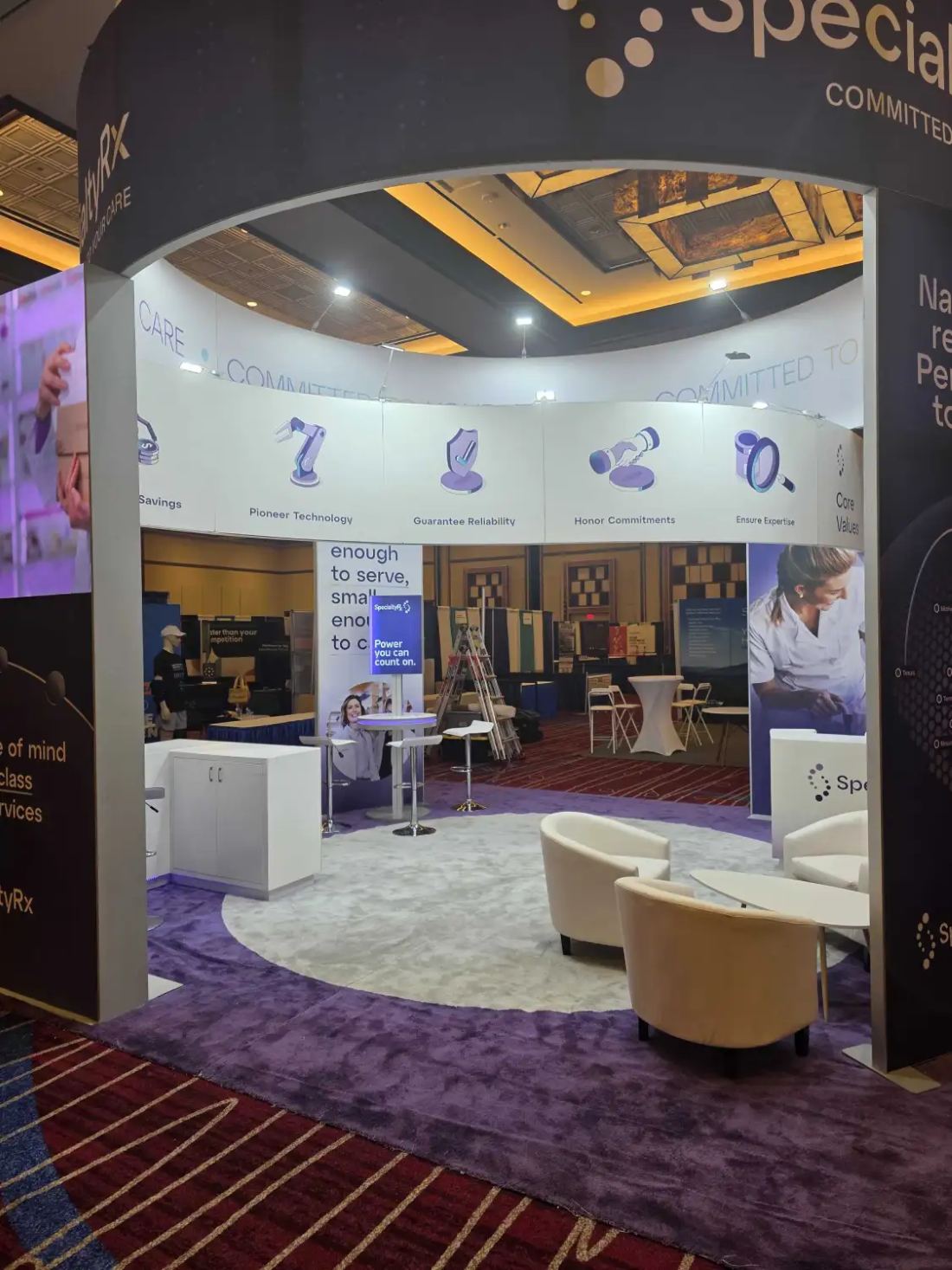 SpecialtyRx 20x20 peninsula trade show booth with a curved archway entrance, icon graphic wall, lounge seating and purple carpet