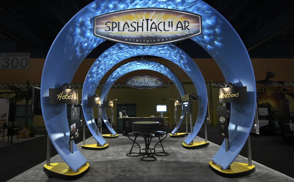 Splashtacular 20x20 peninsula trade show exhibit with three illuminated blue arches, lit product kiosks and a central meeting table