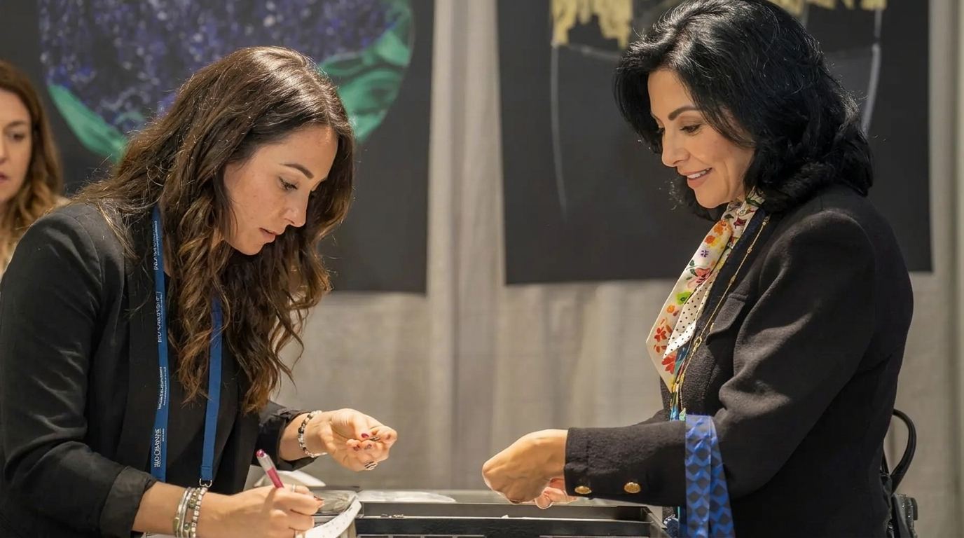Booth rep in a black blazer writing up an order with a buyer at a jewelry counter, the kind of booth staff Purple books for St. Louis trade shows