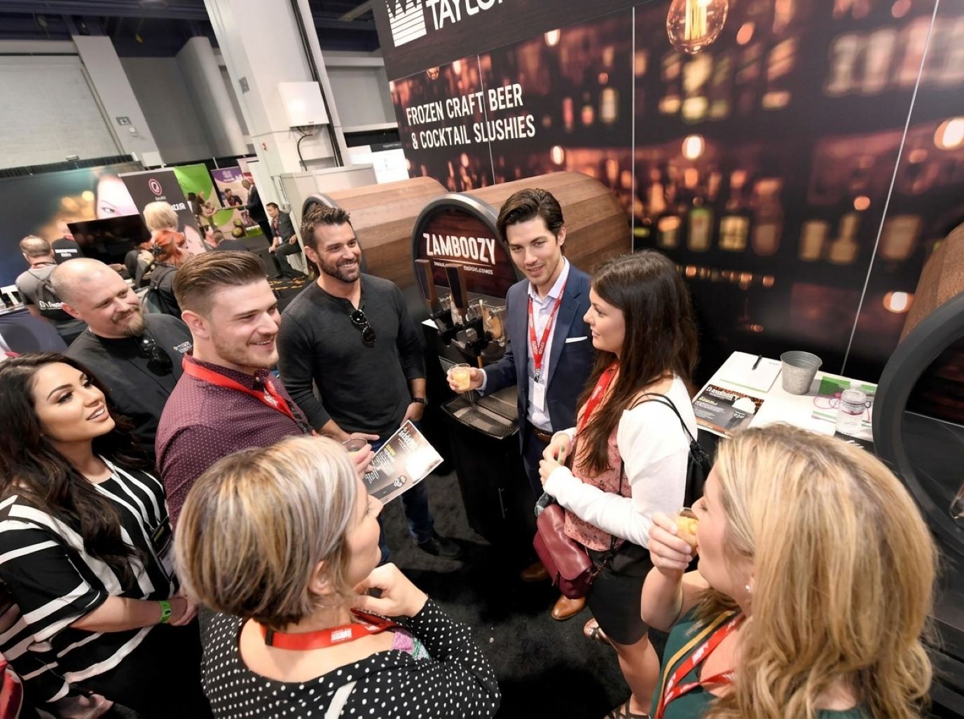 Booth host in a navy blazer pouring frozen drink samples for a crowd of buyers at a beverage dispenser, the kind of sampling crew Purple sends to National Restaurant Association Show booths