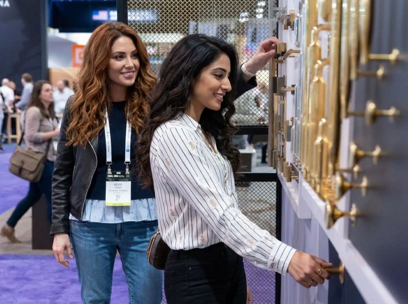 Product presenter in a pinstripe blouse trying brass cabinet pulls with a badged visitor at a hardware display wall