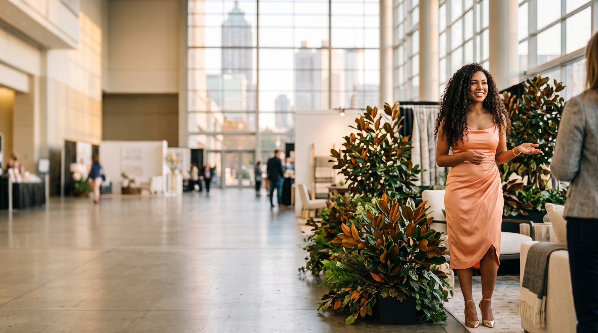 Showroom host in a peach satin dress welcoming buyers among magnolia arrangements at a downtown Atlanta market showroom